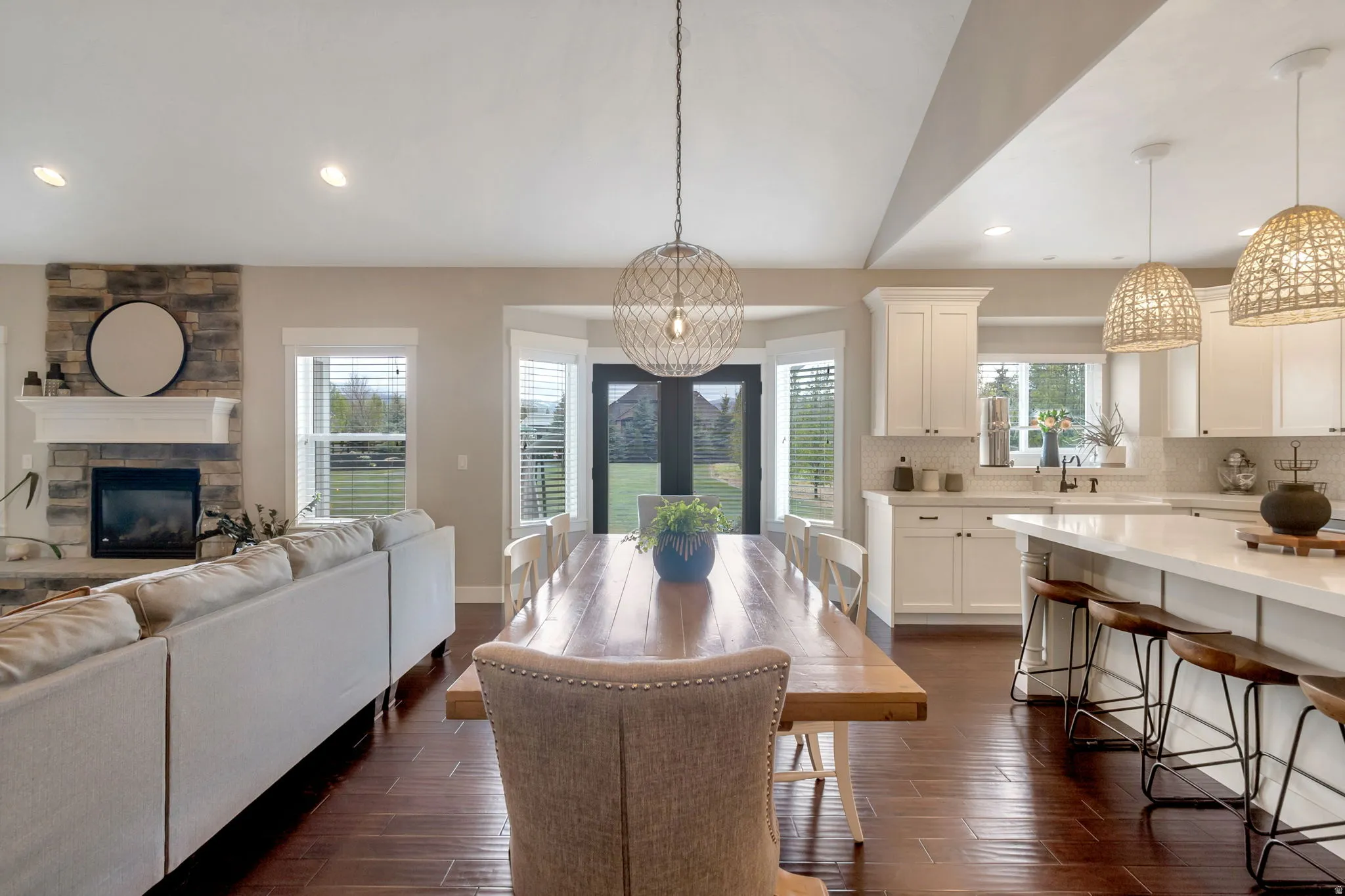 Open-concept living space featuring wood-finish flooring, a stone-faced fireplace with a white mantel, and vaulted ceilings