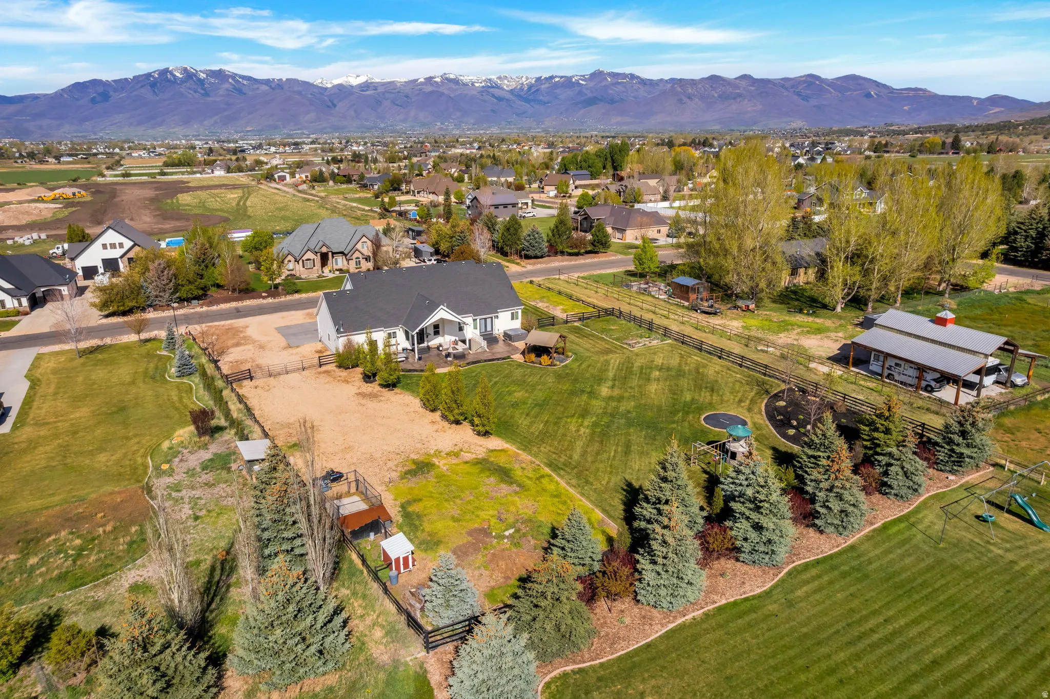 Spacious property featuring a white exterior residence with a dark roof, a large rear deck, an expansive lawn, and mature trees