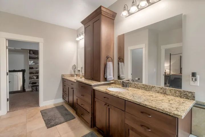 Bathroom featuring a dual vanity with granite countertops, rich wood cabinetry, and a full-width mirror