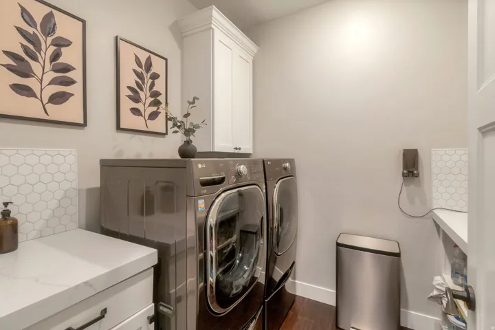 Laundry area featuring wood-finish flooring, white cabinetry, hexagon tile backsplash, and a white countertop