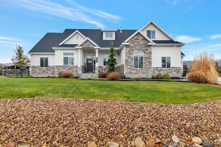 Contemporary residence featuring a striking stone and siding exterior, a dark shingle roof, a covered front porch, and a well-maintained lawn with mature landscaping