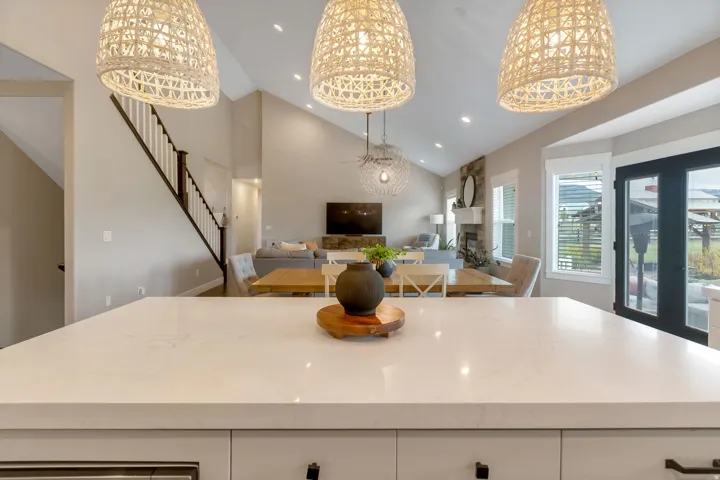 Kitchen island featuring a light-toned countertop, three woven pendant lights, vaulted ceilings, a stone fireplace, and double exterior doors