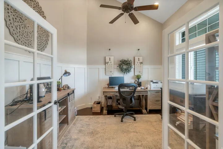 French doors opening into a dedicated room with a high vaulted ceiling, wood-finish flooring, a ceiling fan, and board and batten wainscoting