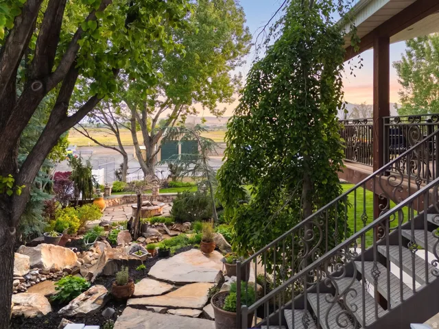Tiered outdoor living space featuring an ornate wrought iron staircase and balcony railing, flagstone pathway, mature trees, and natural rock landscaping