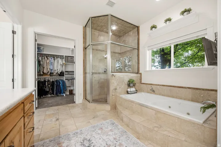 Primary bathroom featuring an enclosed glass shower, a built-in jetted tub, a window with exterior tree scenery, tile flooring, and a walk-in closet with built-in shelving