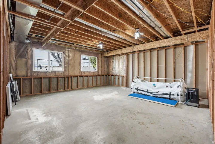 Unfinished basement space featuring exposed wood framing, two windows, concrete flooring, and overhead lighting