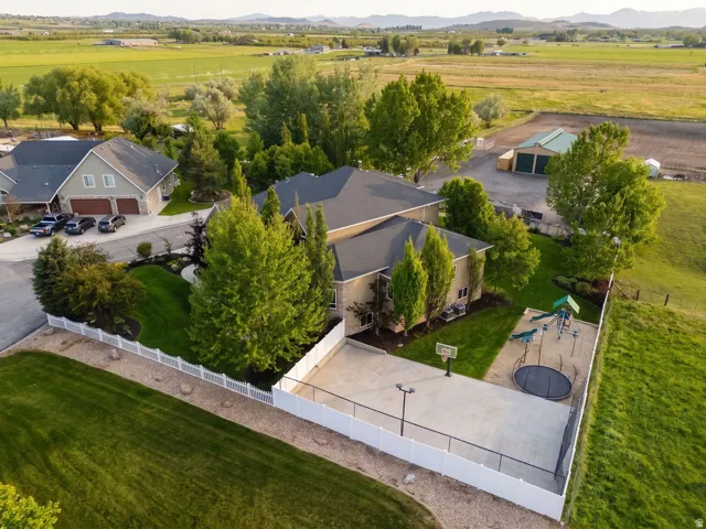 Featuring a paved sports court, playground, manicured lawns, mature trees, and a durable white fence