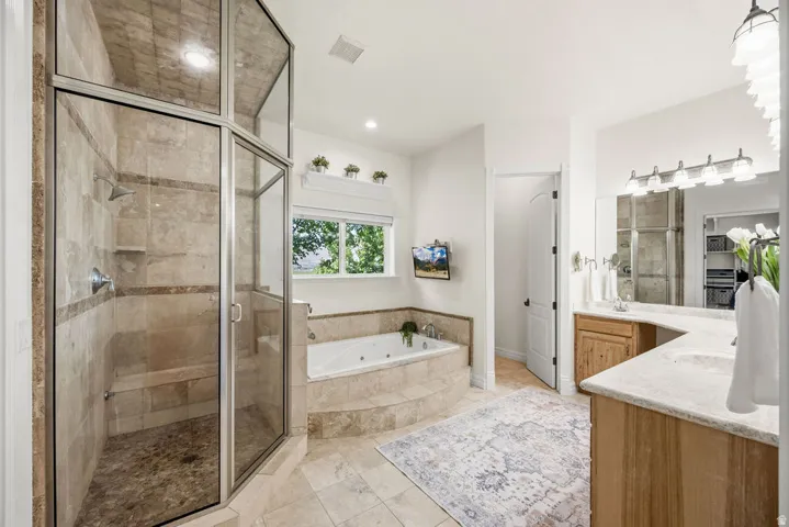 Primary bathroom featuring a glass-enclosed shower with tile surround and built-in bench, a jetted soaking tub, and a double vanity with stone countertops and wood cabinetry