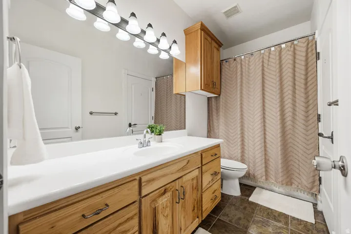 Bathroom featuring a wood-finish vanity with an integrated white sink, bright overhead lighting, and a full-width mirror