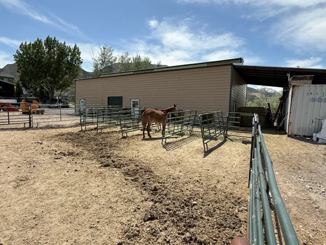 Equestrian facility featuring a metal-sided barn, covered open-air structure, and durable metal corrals