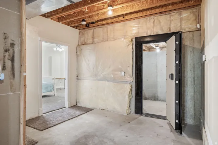 Vault enclosed safe.  Unfinished basement area featuring exposed ceiling joists, concrete flooring, and a heavy-duty vault door