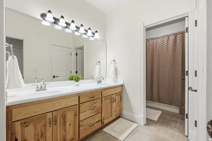 Jack and Jill bathroom double vanity with light wood cabinetry, chrome fixtures, and a spacious mirror