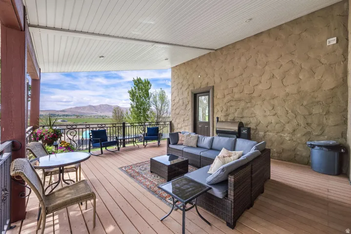 Expansive covered balcony featuring wood-finish decking, a stone-textured exterior wall, white paneled ceiling, and black metal railings