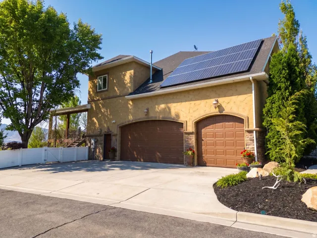 Stucco exterior featuring dual garage doors, solar panels, and a stone accent facade