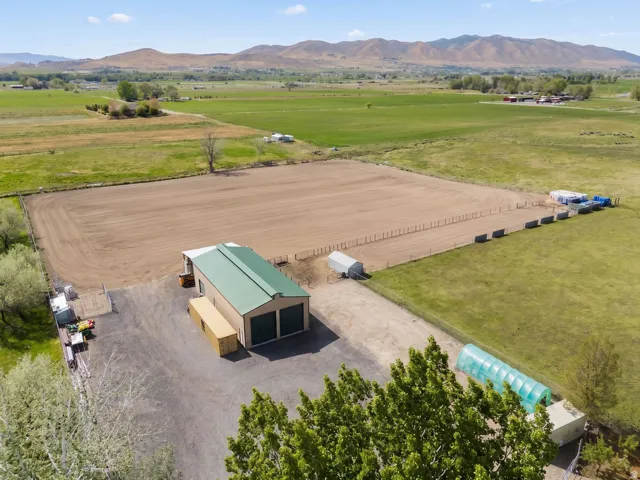 Expansive rural property featuring a large open field, a two-bay detached outbuilding with a green metal roof, and an enclosed greenhouse structure