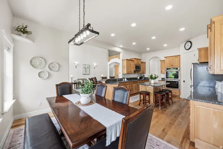 Spacious dining area featuring wood-finish flooring, a contemporary linear chandelier, and archway architectural details