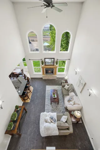 Two-story living area featuring a vaulted ceiling with a ceiling fan, a fireplace with a wood mantle, and a series of arched windows