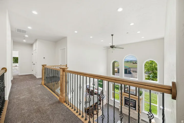 Upper-level landing featuring wood handrails with wrought iron balusters, recessed lighting, and carpet flooring