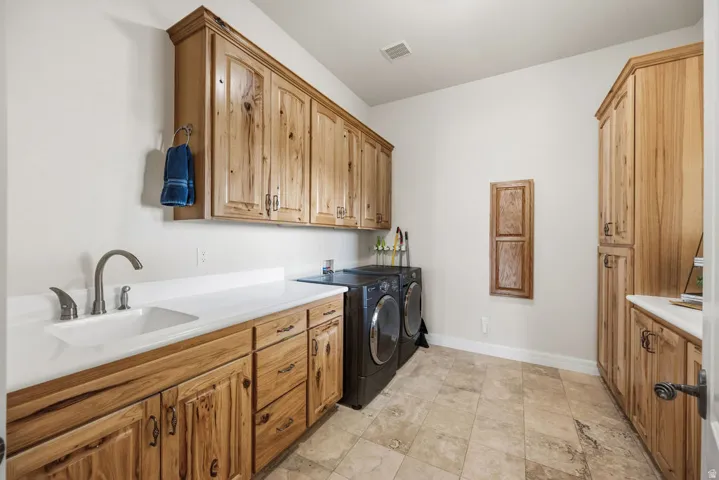 Spacious utility room featuring extensive natural wood cabinetry, a built-in sink with a gooseneck faucet, light-toned countertop space, and tile flooring