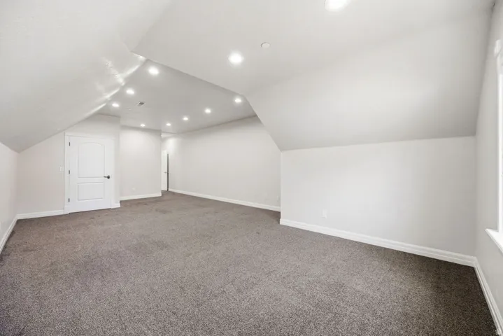 Spacious room featuring vaulted ceilings, recessed lighting, neutral tone carpeting, white baseboards, and a white two-panel arched door