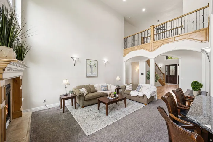 Vaulted living area featuring a fireplace with a decorative mantel, an upper-level balcony with iron railings, arched doorways, and wood-finish flooring
