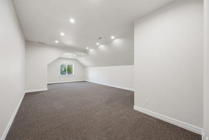 Spacious room featuring vaulted ceilings, recessed lighting, a window with exterior views, and neutral-toned carpeting