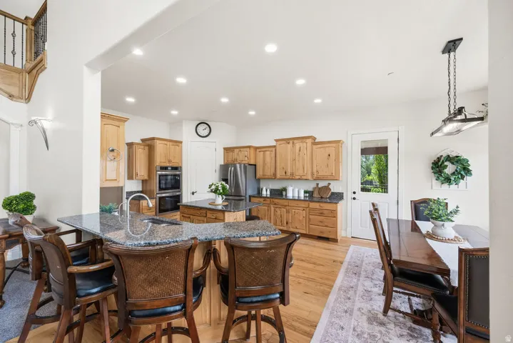 Kitchen featuring stone countertops, integrated double ovens, stainless steel refrigerator, and wood-finish flooring