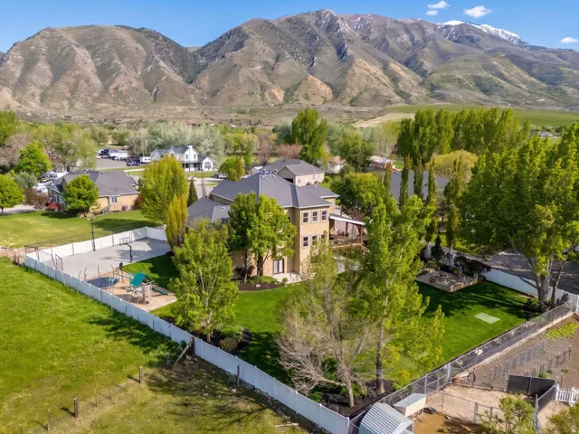 Spacious property featuring a large home with a covered patio, expansive manicured lawns, a fenced multi-sport court, and mature trees