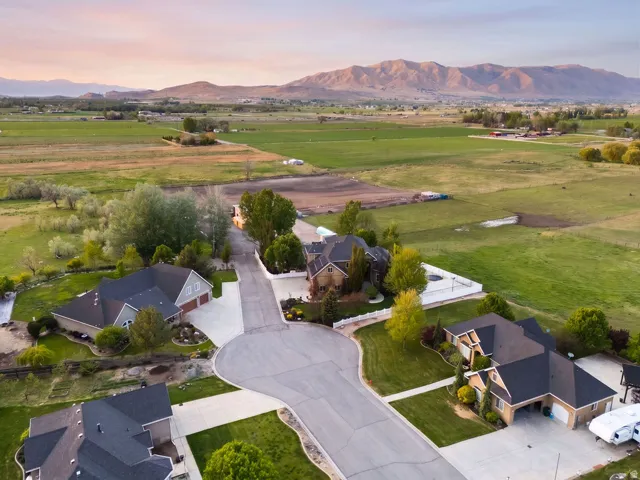 Residential cul-de-sac with mature landscaping, surrounded by expansive green fields and distant mountains
