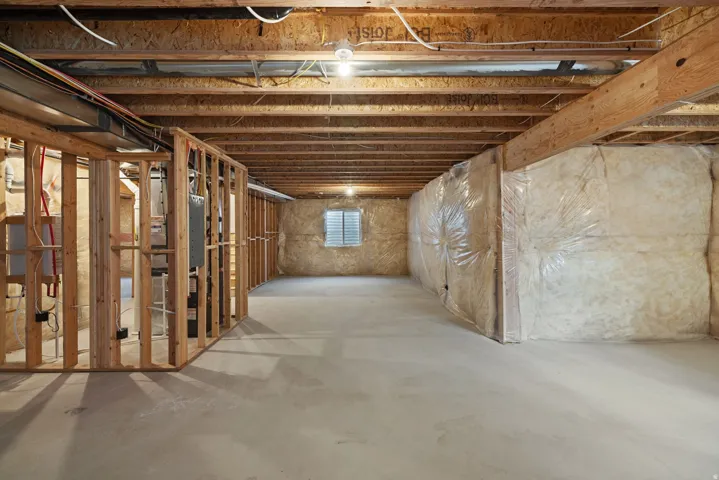 Unfinished basement featuring concrete flooring, exposed wood framing, and a visible window