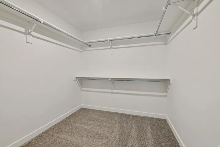 Walk-in closet featuring light-colored carpeting, white baseboards, and multiple levels of shelving and hanging rods