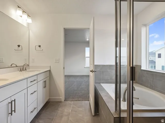 Bathroom featuring a double vanity with white cabinetry, a built-in bathtub with tile surround, a glass-enclosed shower, and tile flooring