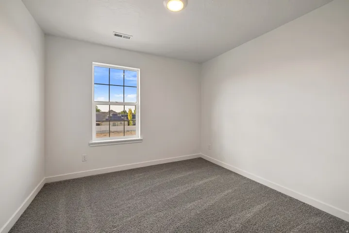 Windowed room featuring textured gray carpeting, white walls, and bright overhead lighting