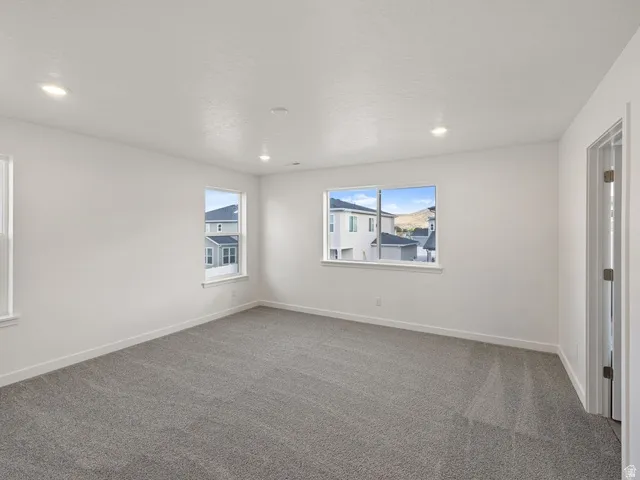 Spacious room featuring neutral grey carpeting, white walls, multiple windows with white trim, and recessed lighting