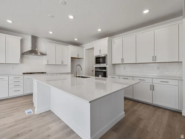 Kitchen featuring a large central island with a solid surface countertop, white shaker cabinetry, stainless steel appliances, a subway tile backsplash, and light wood-finish flooring