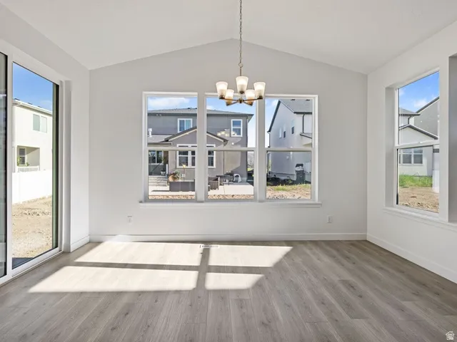 Vaulted ceiling dining area featuring wood-finish flooring, a contemporary chandelier, multiple windows, and a sliding glass door