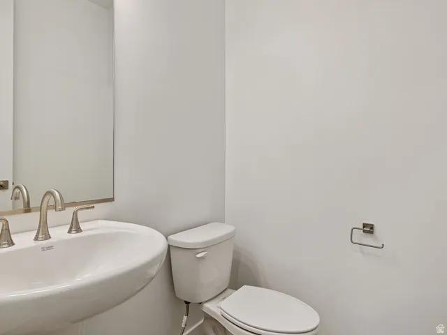 Powder room featuring a pedestal sink with brushed nickel faucet, wall-mounted mirror, and a white toilet