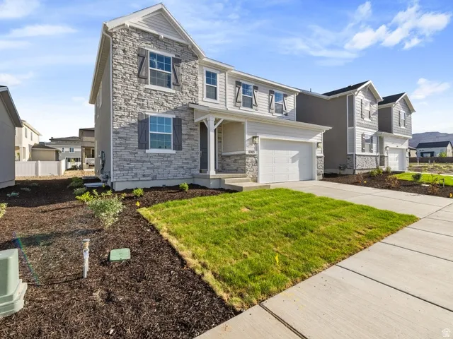 Contemporary two-story residence featuring a stone and siding exterior, an attached two-car garage, a covered front porch, and a newly seeded lawn with landscaped beds