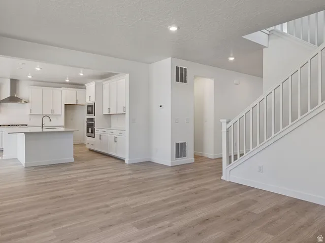 Open-concept living space featuring wood-finish flooring, a contemporary staircase with white balusters, and recessed lighting