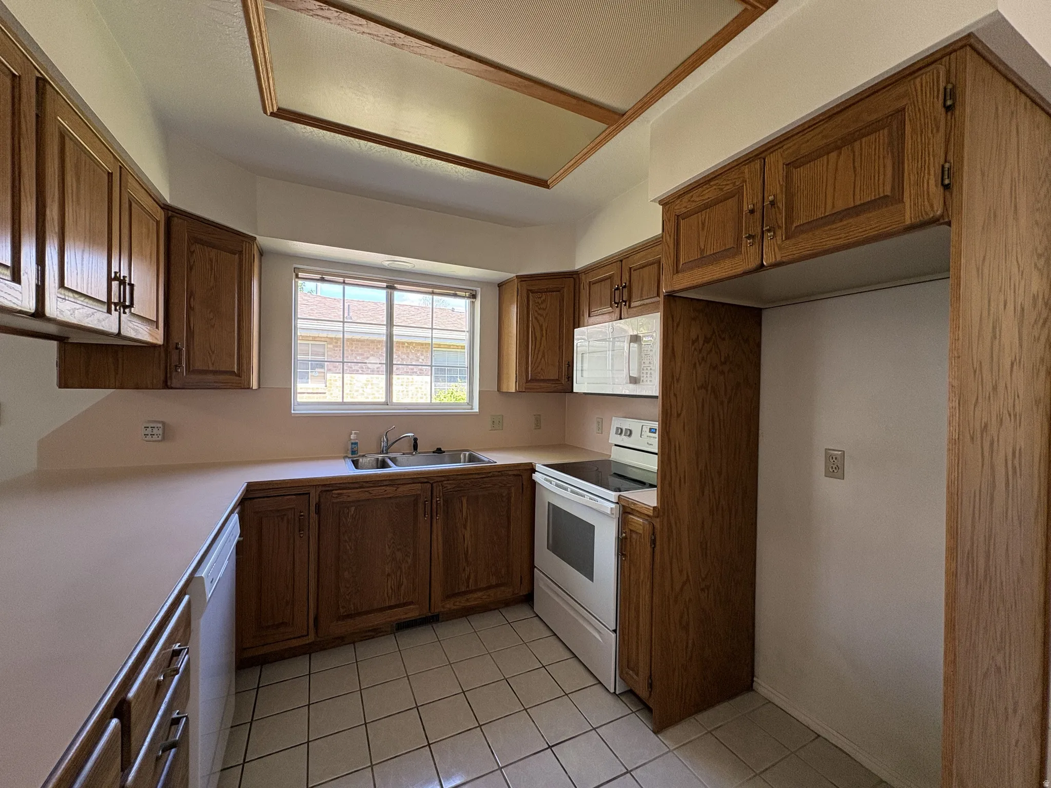 Kitchen with wood-finish cabinetry, solid surface countertops, and white tile flooring