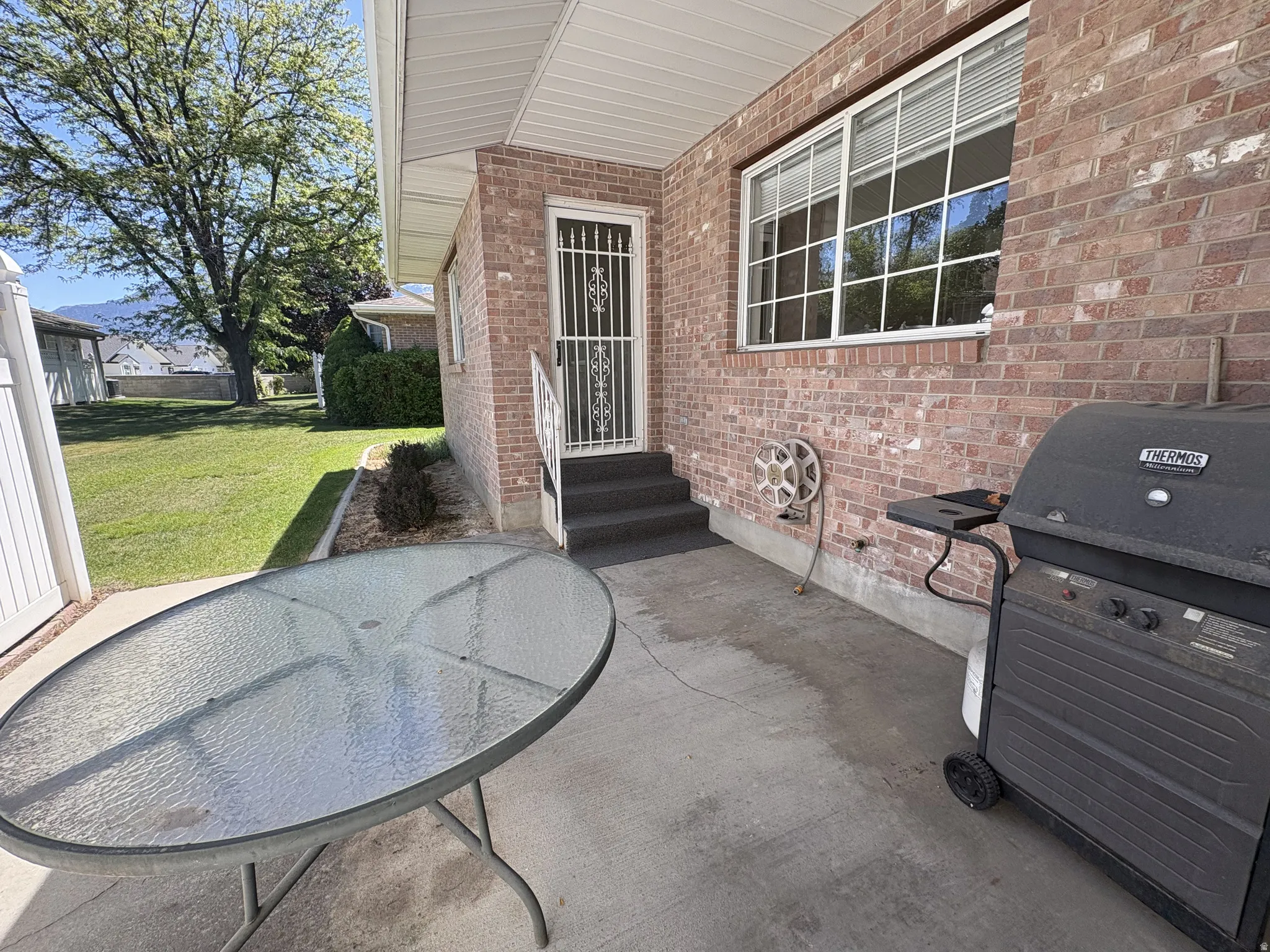 Paved patio area featuring a brick exterior wall, a large gridded window, and a white security screen door