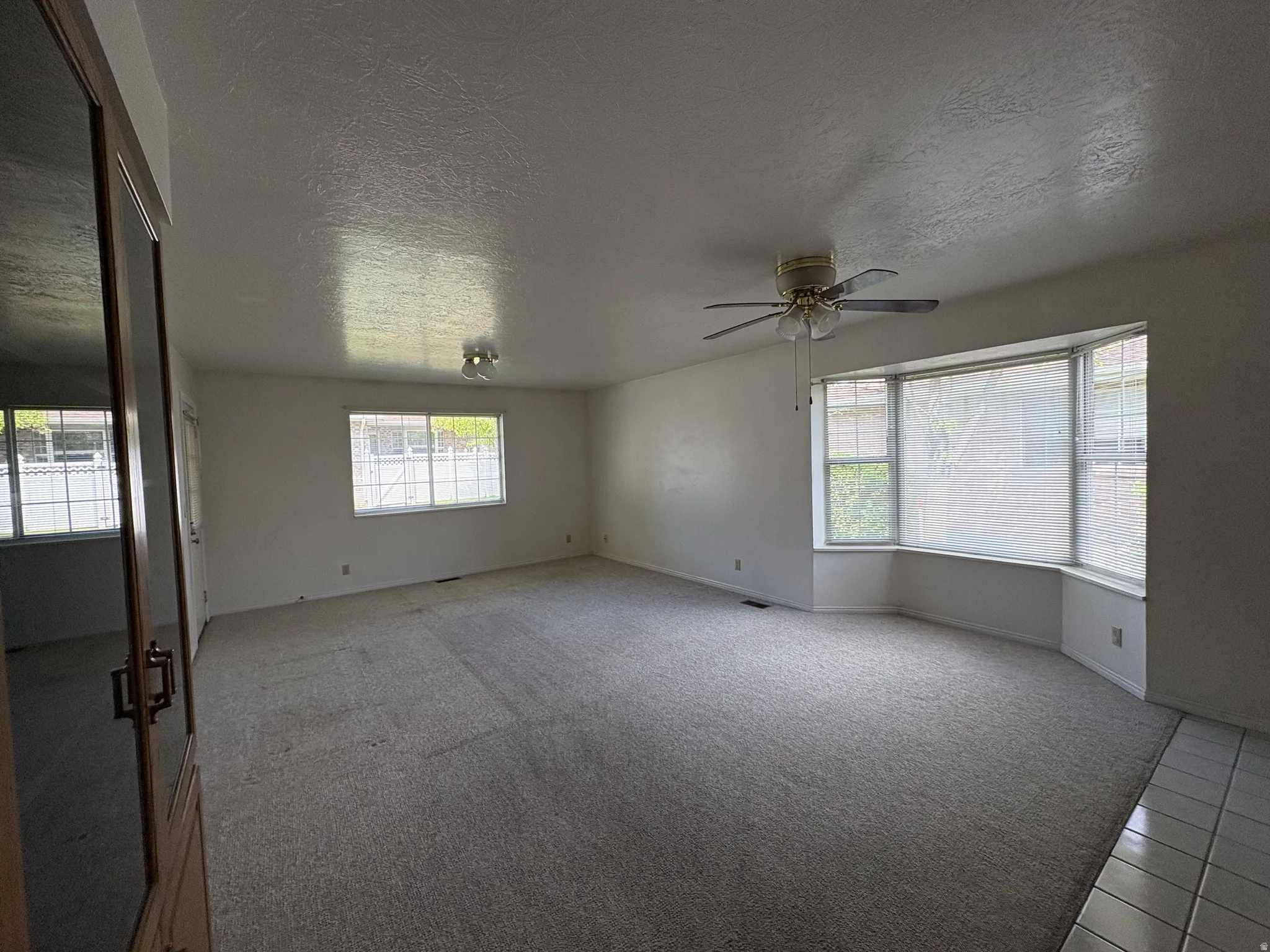 Spacious interior room featuring a large bay window, light gray carpet, and white walls