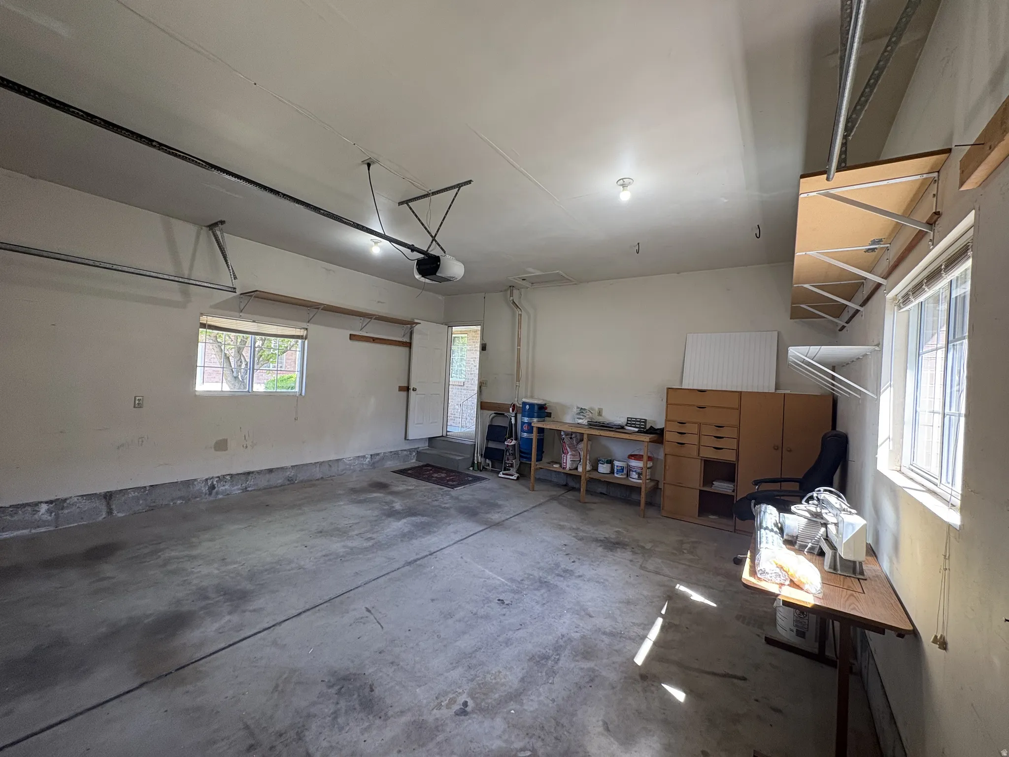 Spacious garage featuring a concrete floor, two windows providing natural light, overhead lighting fixtures, and an automatic garage door opener