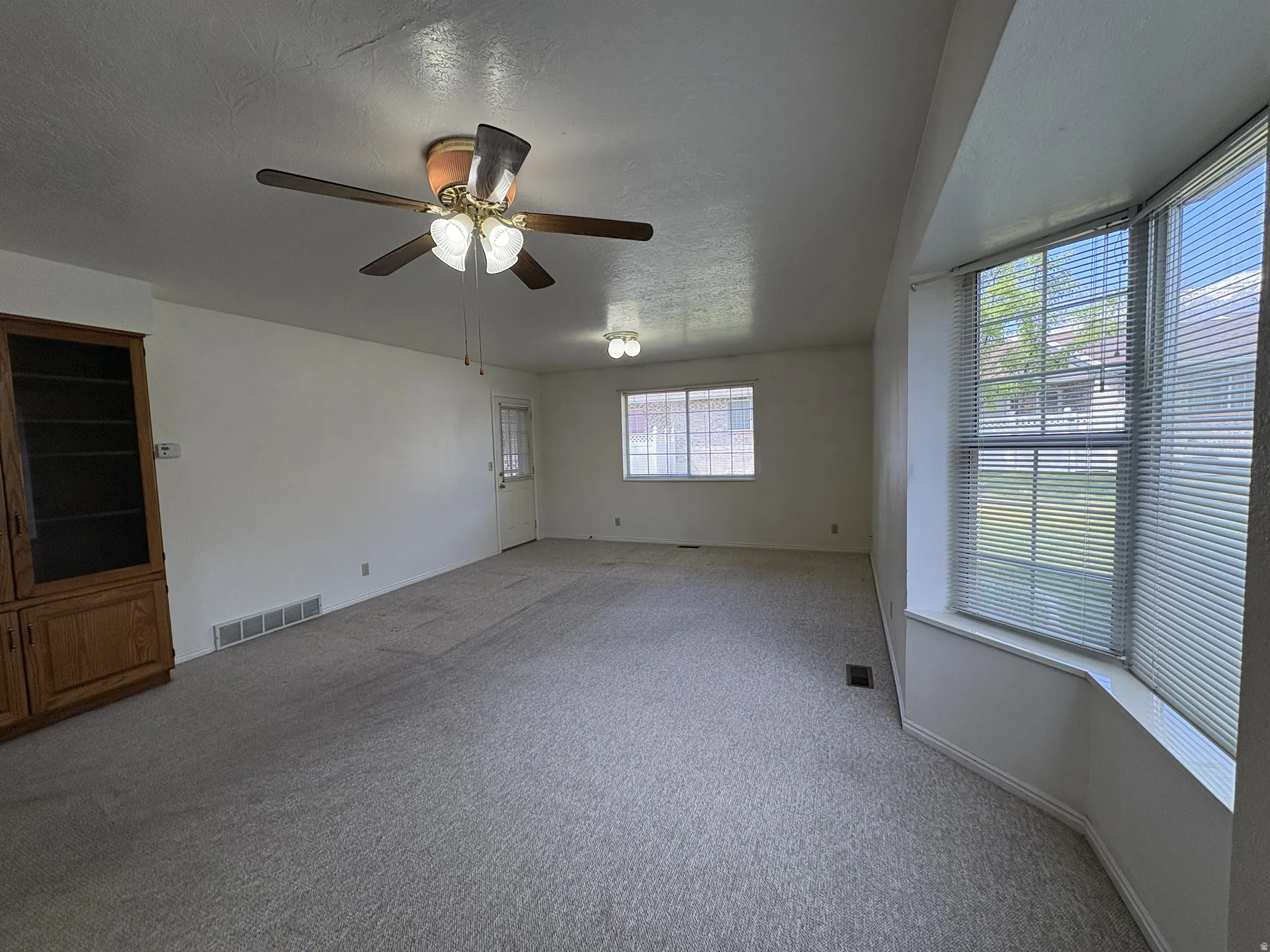 Spacious living area featuring light-toned carpeting and a ceiling fan with integrated lighting