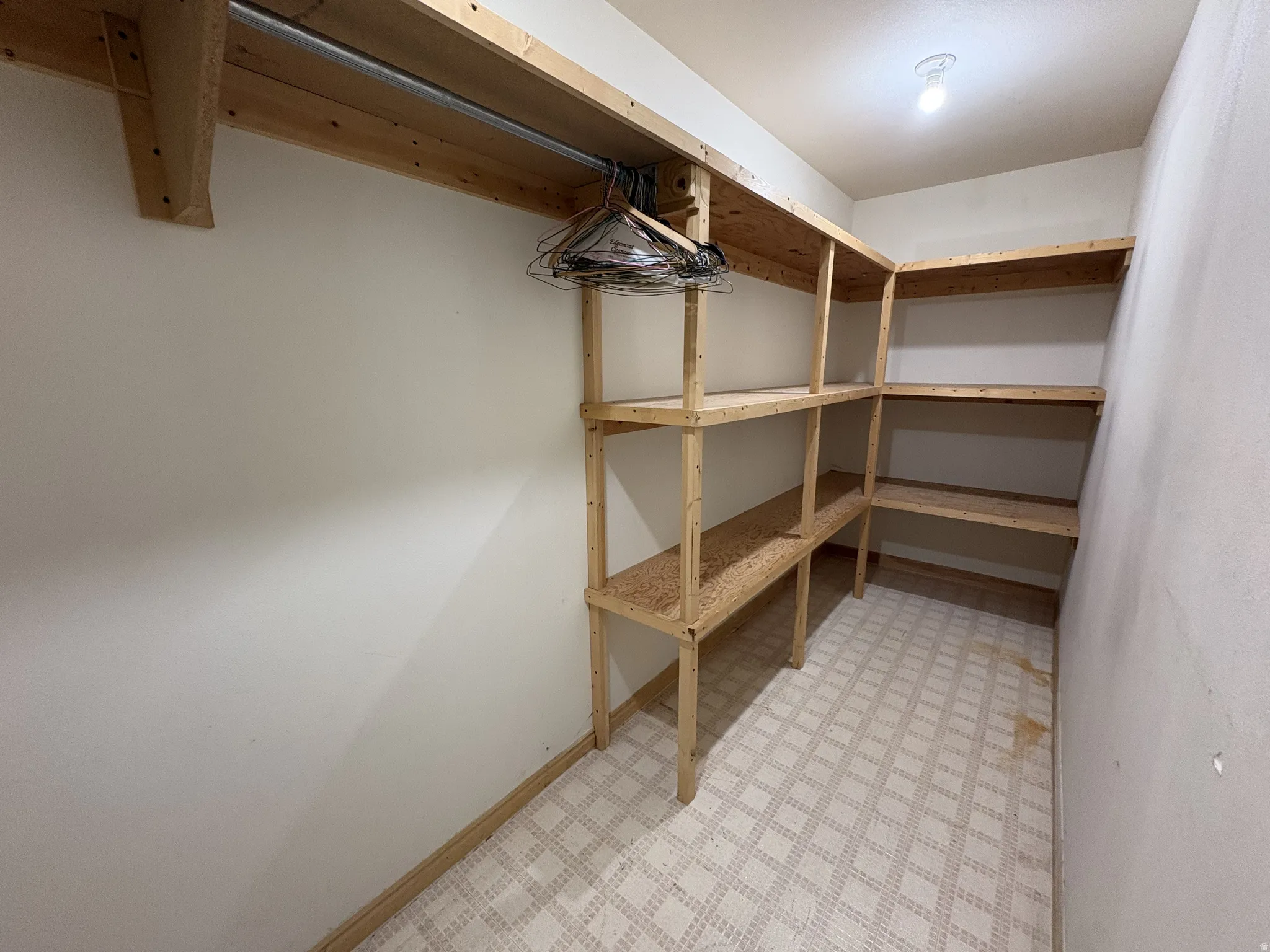 Storage room with patterned flooring, built-in wooden shelving, and a hanging rod