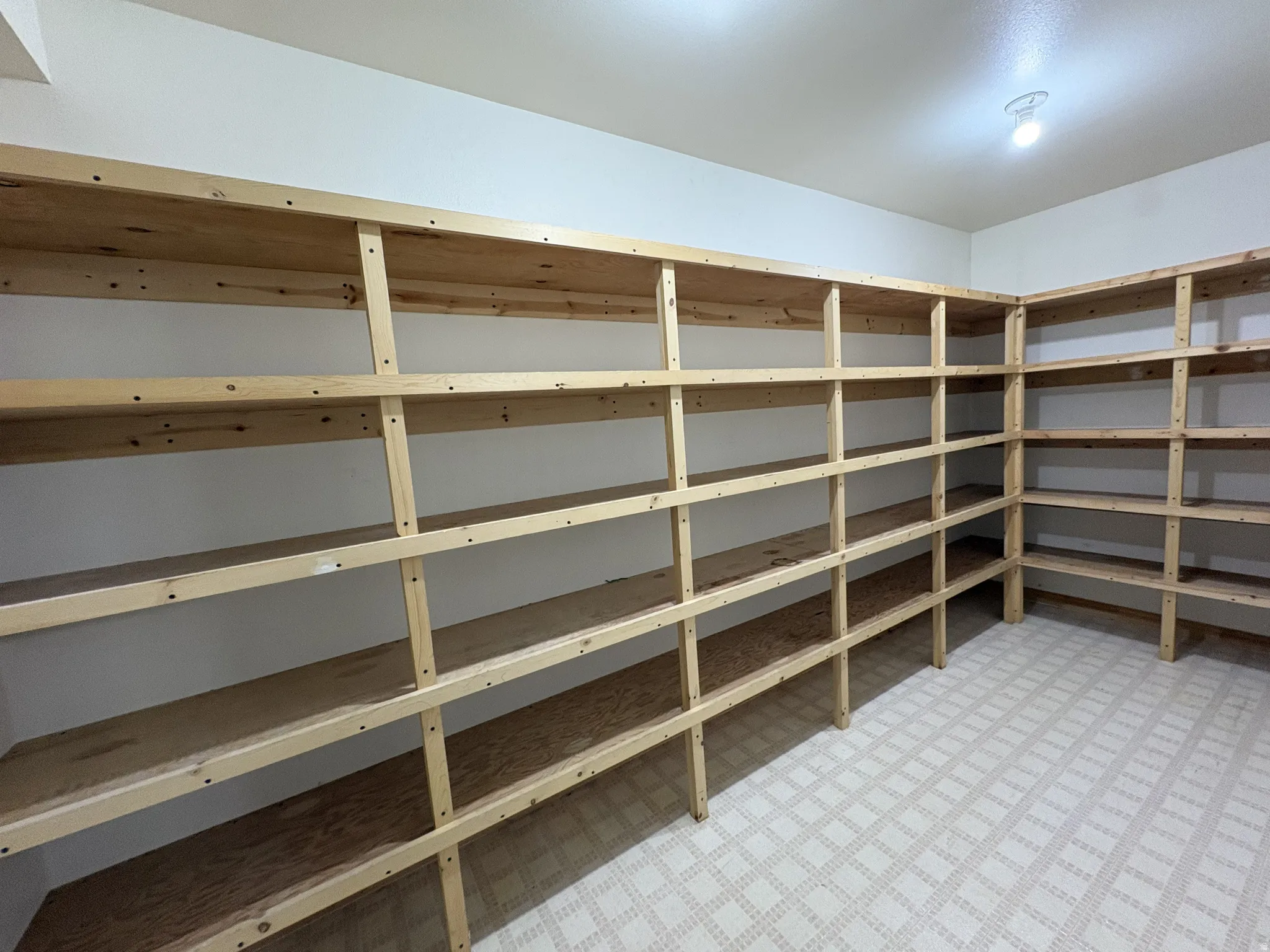 Dedicated storage room featuring extensive built-in wooden shelving, white painted walls, and patterned vinyl flooring