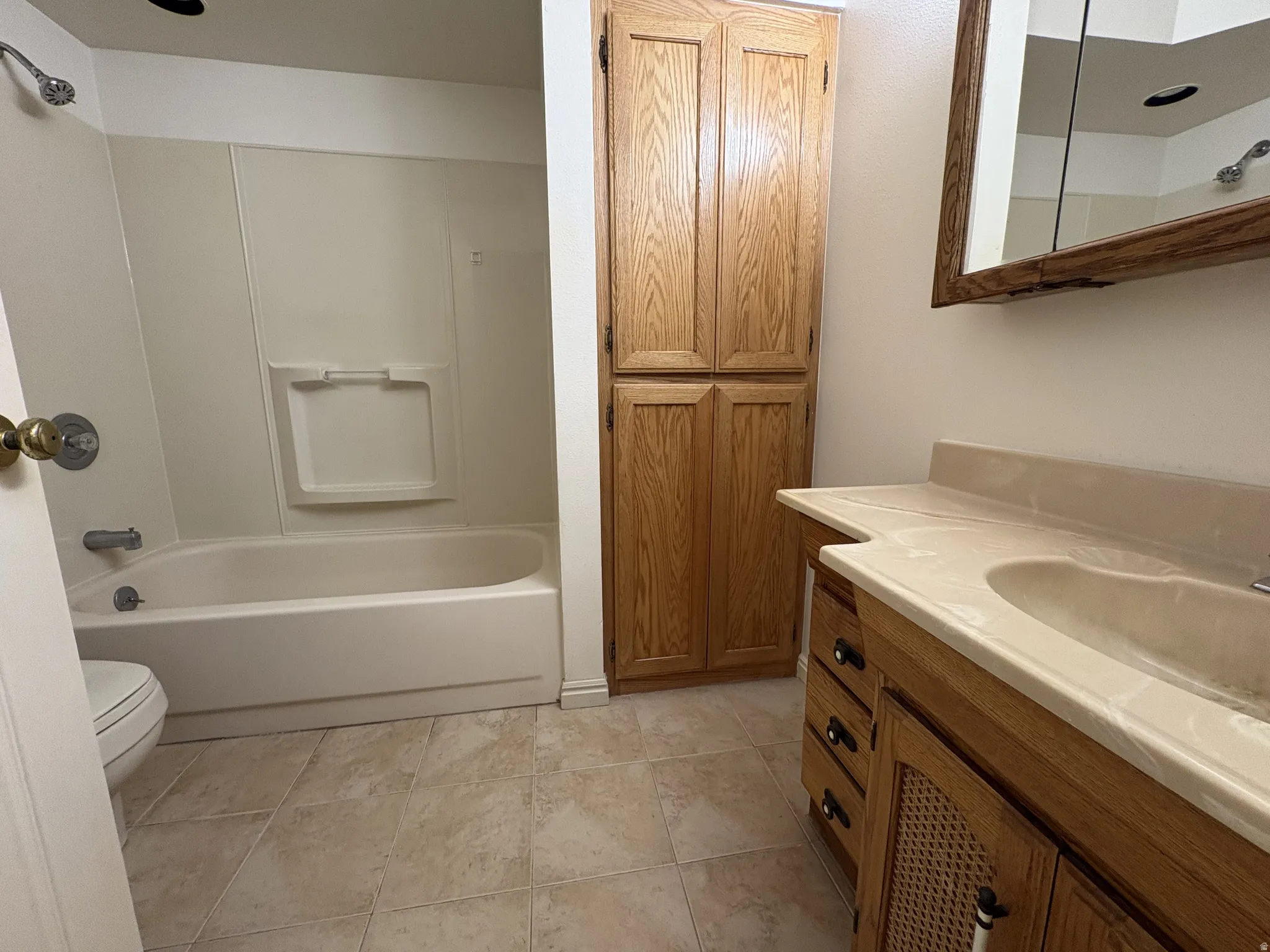 Full bathroom featuring a single vanity with integrated sink, wood-finish cabinetry, built-in shelving, a shower/tub combination, and tiled flooring