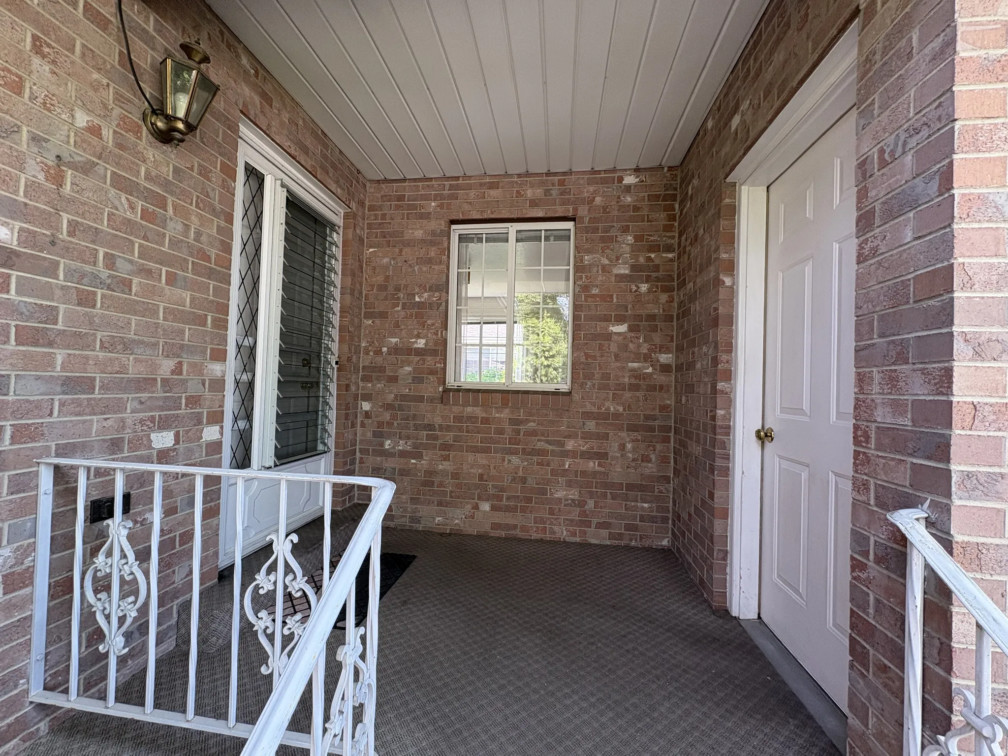Covered front porch featuring a brick facade and white railing