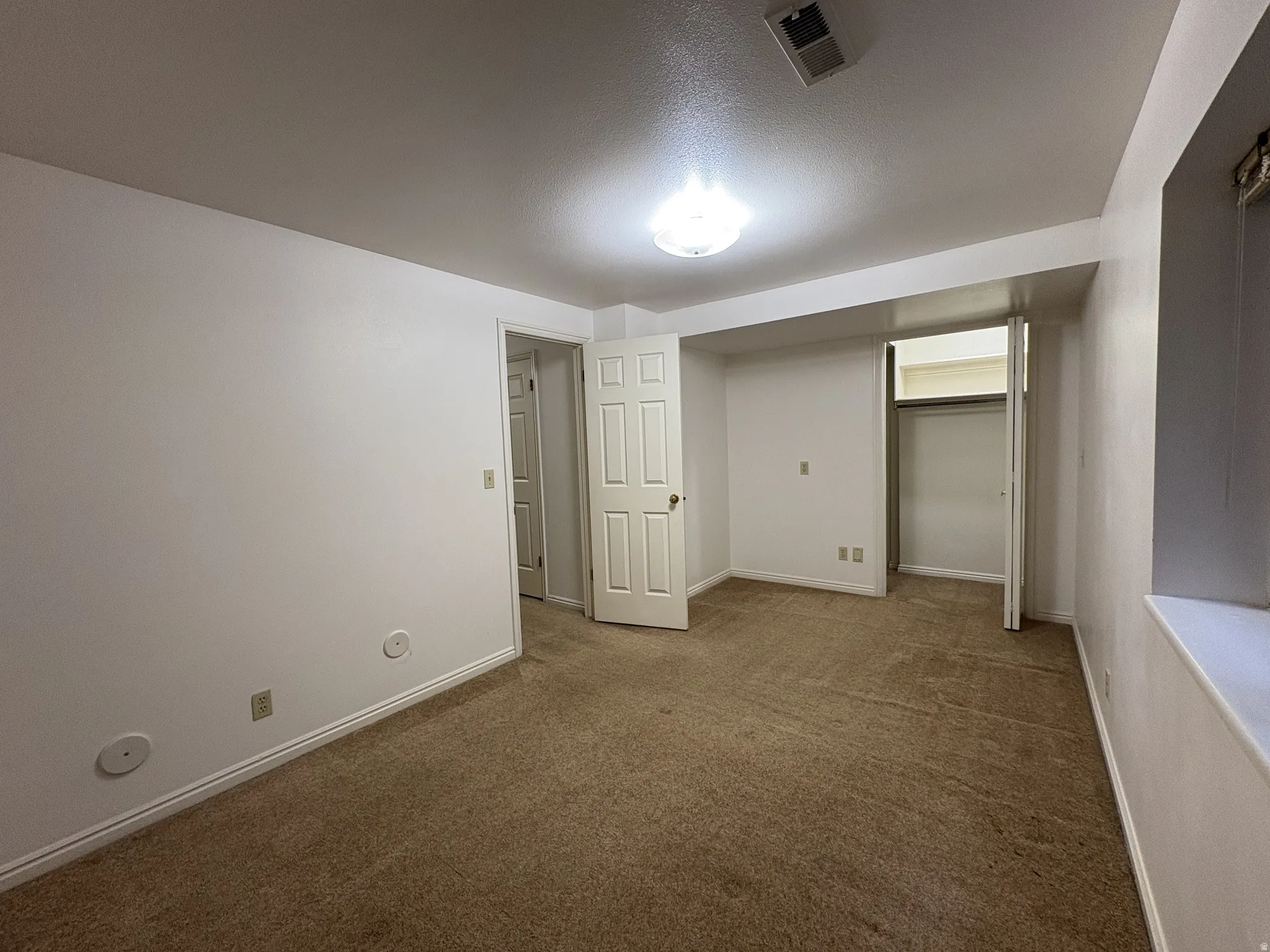 Carpeted room featuring white walls, white trim, a flush-mount ceiling light, a built-in closet with bifold doors, and a window well