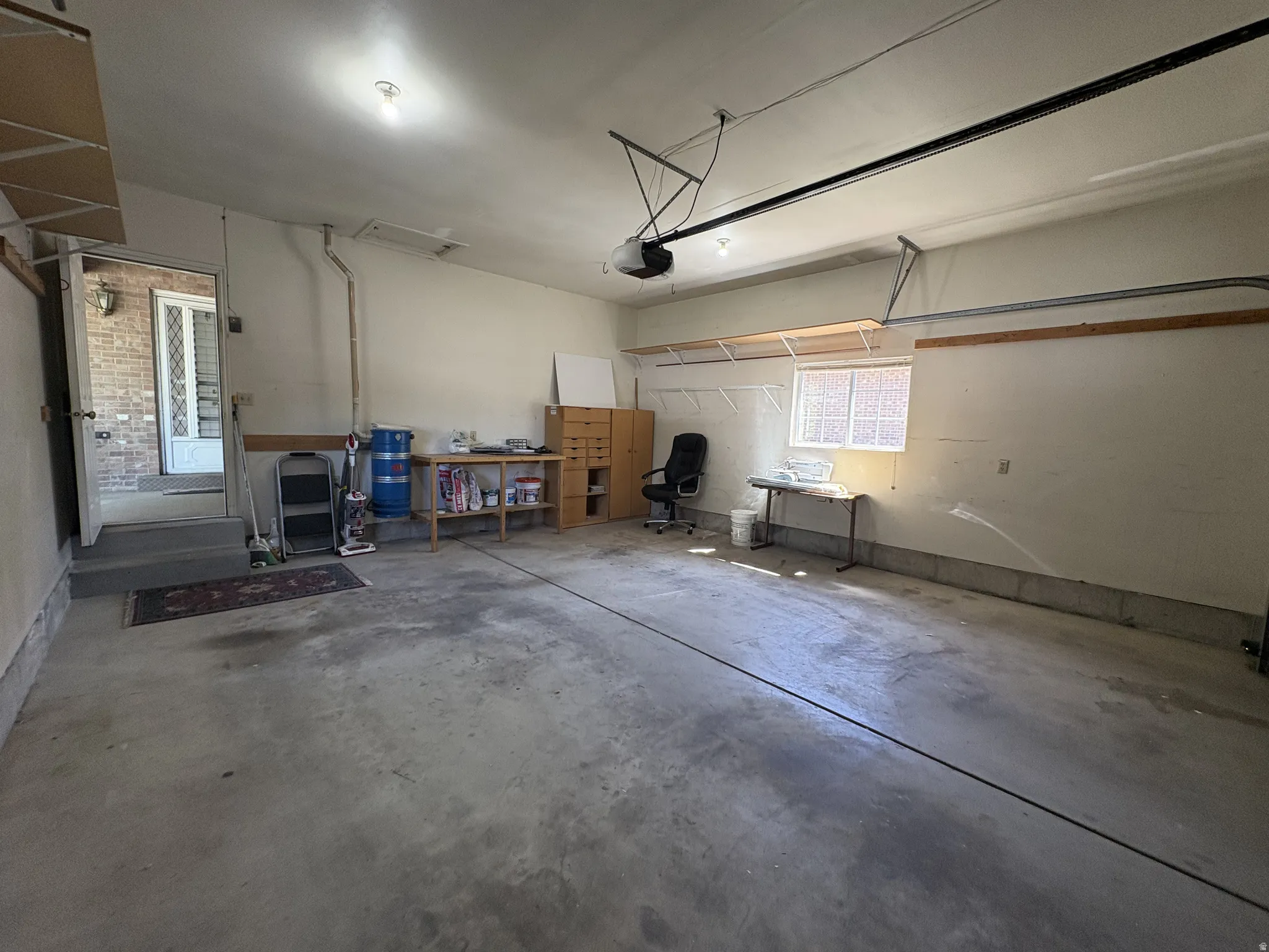 Spacious 2 car garage featuring a concrete floor, overhead lighting, an interior access door, a transom window, and built-in shelving